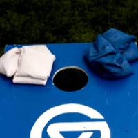 Cornhole setup: blue painted pallet with white GV logo, white beanies in the left corner and blue beanies in the right corner